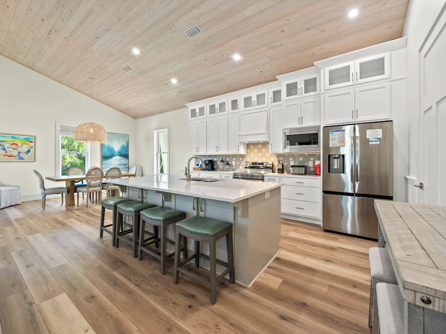 Una cocina moderna con armarios blancos, una isla grande con taburetes de bar, electrodomésticos de acero inoxidable y techo de madera.