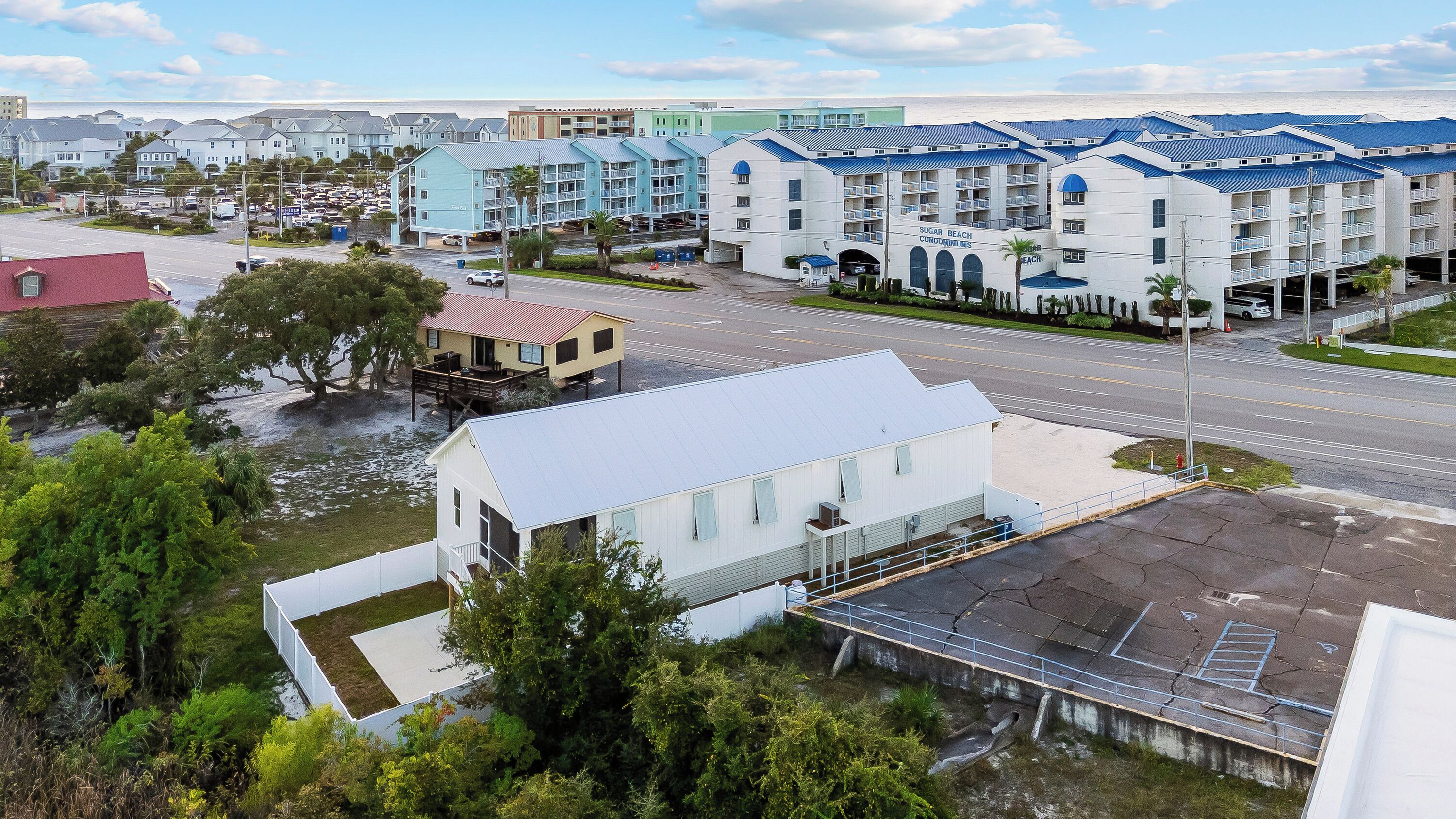 A coastal residential area with modern buildings, a parking lot, and a road.