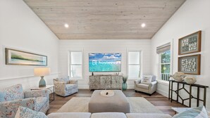 A spacious living room with a large flat-screen TV, a sofa set, a coffee table, and a decorative cabinet. - Luxury 4BR | Across street from beach | New Hot Tub! (Orange Beach)