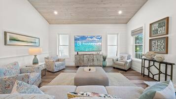 A spacious living room with a large flat-screen TV, a sofa set, a coffee table, and a decorative cabinet.