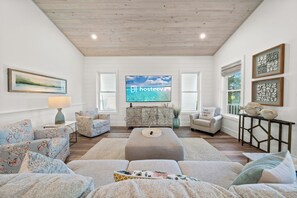 A spacious living room with a large flat-screen TV, a sofa set, a coffee table, and a decorative cabinet. - Luxury 4BR | Across street from beach | New Hot Tub! (Orange Beach)