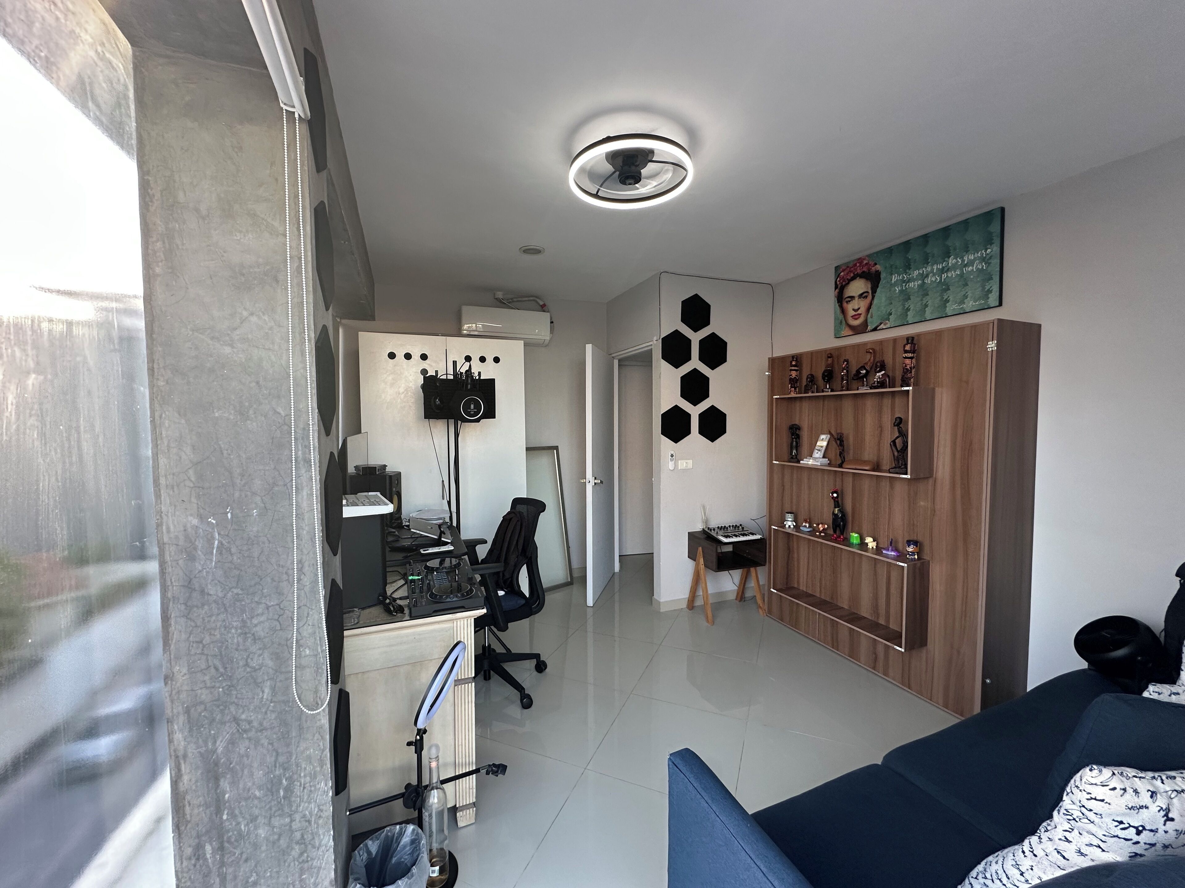 A modern office space with a desk, computer, and chair. There is a bookshelf with decorative items and a painting on the wall.