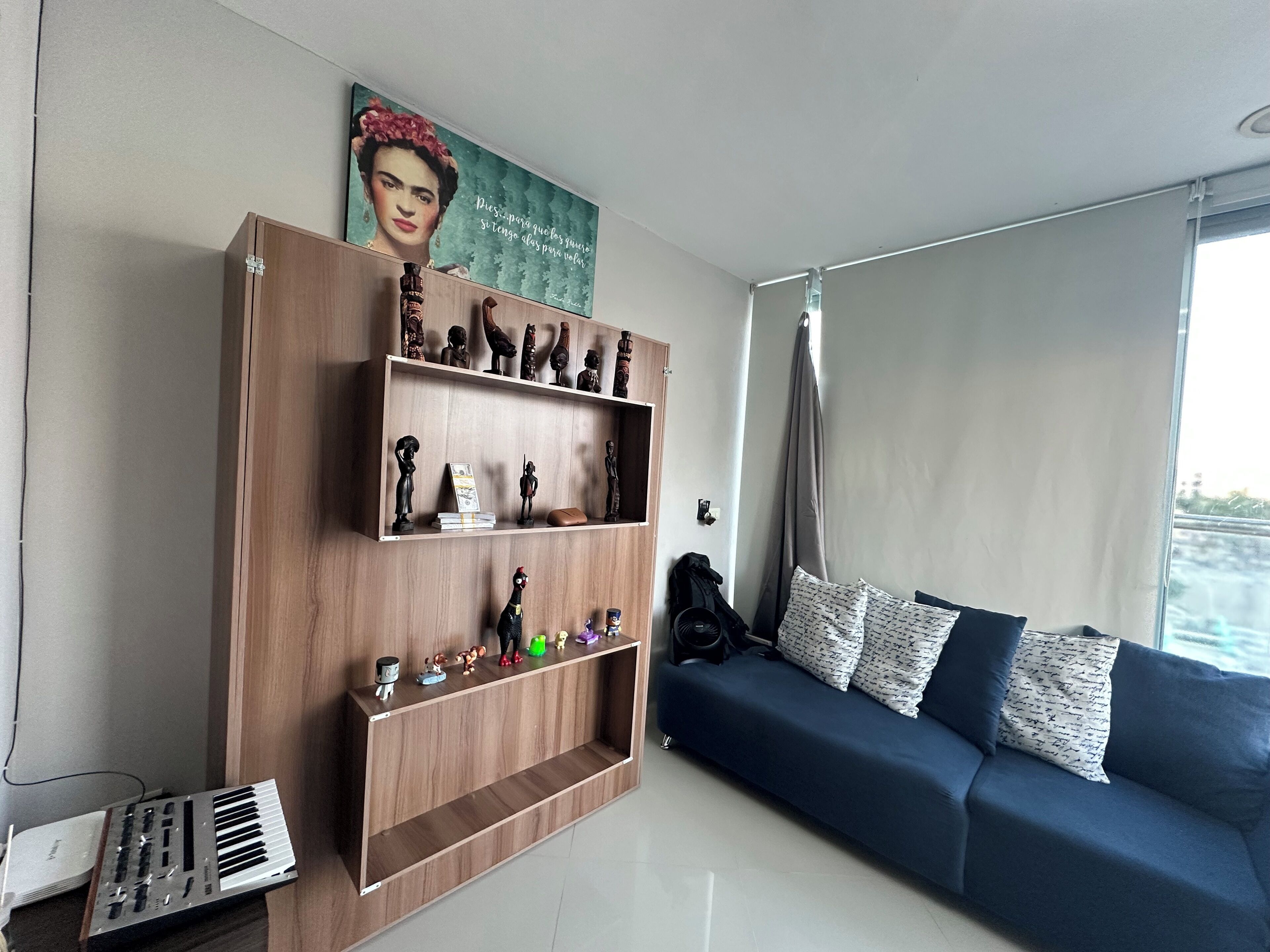 A living room with a blue sofa, a wooden shelf with figurines, a keyboard, and a poster on the wall.