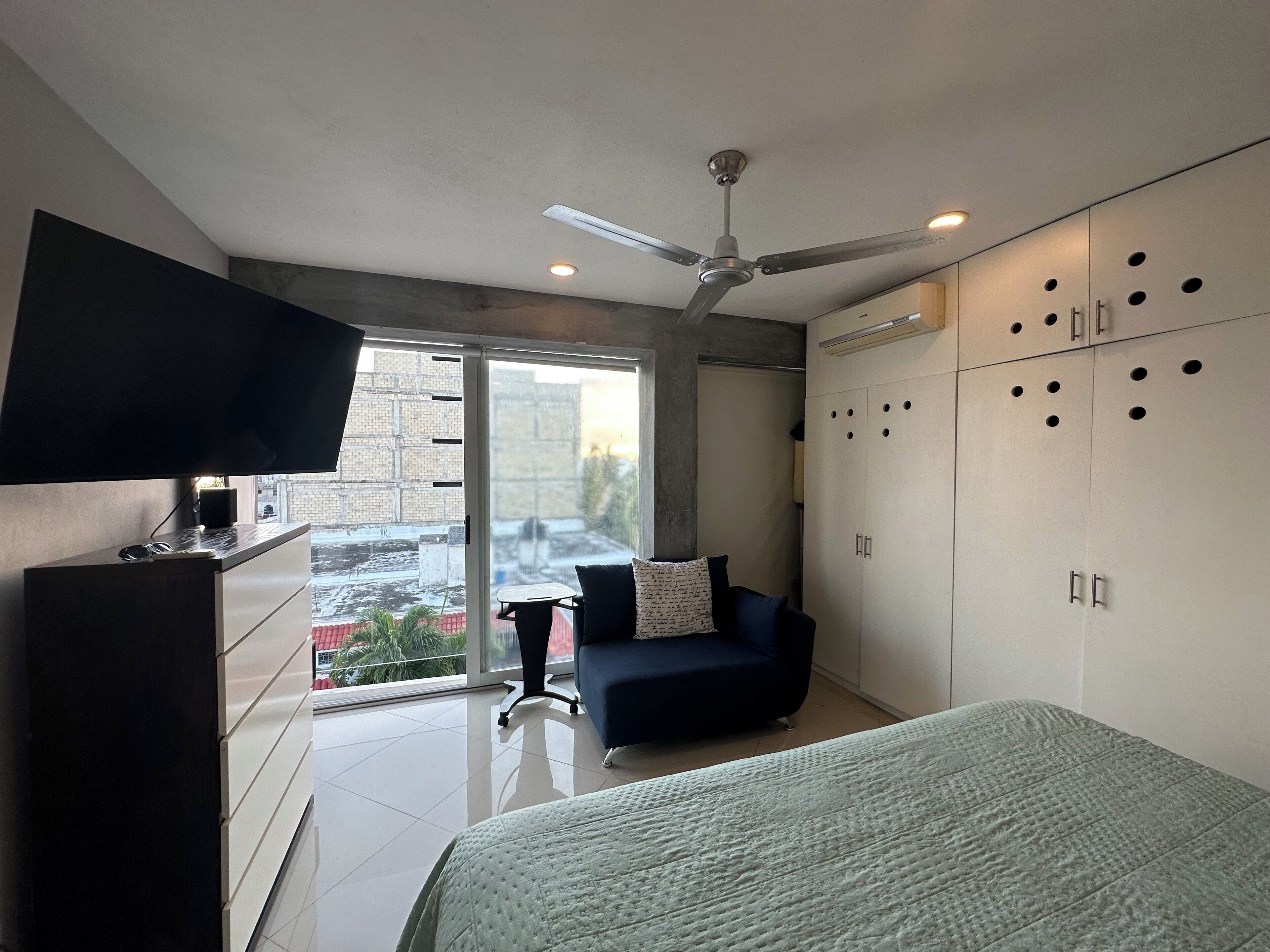 A modern bedroom with a bed, a TV on a stand, a ceiling fan, and a large wardrobe with multiple doors.