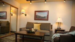 A living room with a sofa, a coffee table with fruit, a lamp, and a painting on the wall. - Ski-in-ski-out Snowbird, X-large studio, Alta, LCC Hot Tub, Heated Pool (Snowbird)