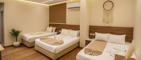 A hotel room with two beds, a potted plant, and a dreamcatcher on the wall.