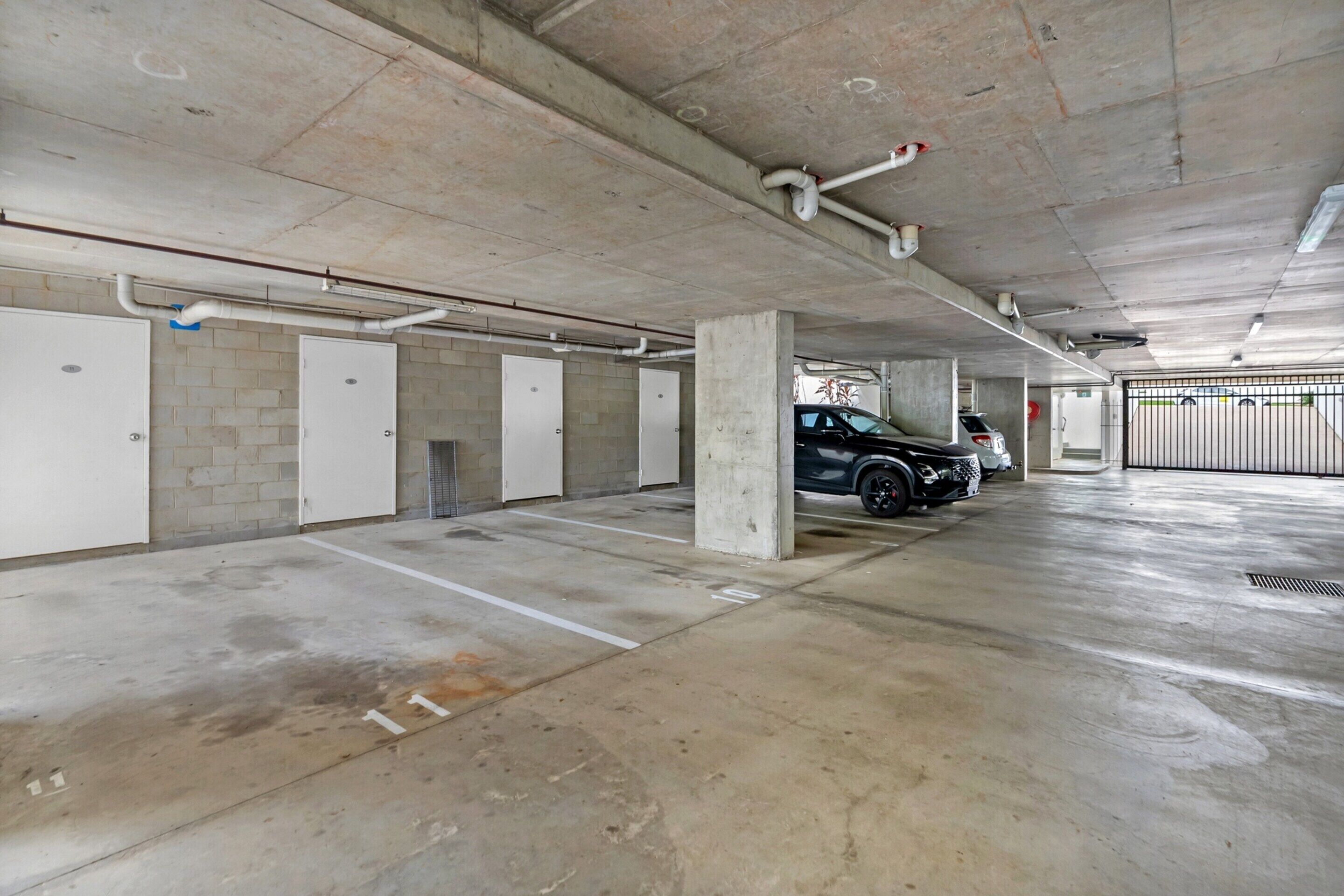 Un aparcamiento de varios niveles con pilares de hormigón, puertas blancas y plazas de aparcamiento delimitadas.