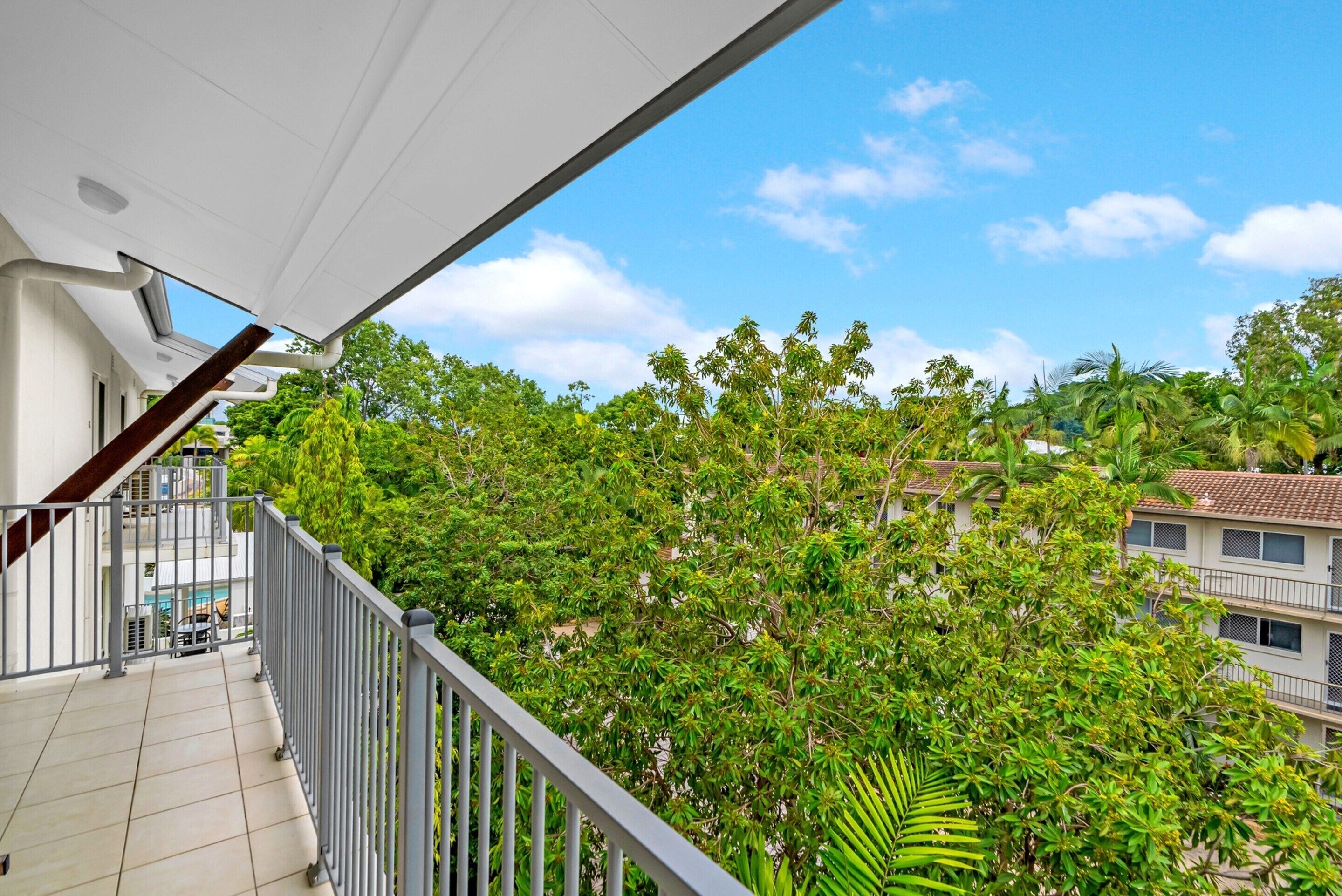 A balcony with a view of lush green trees and a clear blue sky.