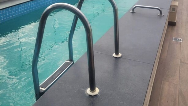 Una piscina en la azotea con barandillas metálicas y vistas a un paisaje urbano.