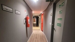 Un pasillo con indicaciones de dirección, un extintor y señalización de salida de emergencia.