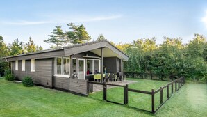 A modern, single-story building with a covered patio area, surrounded by a fenced yard and lush greenery. - "Sjarlotte" - 400m to the fjord by Interhome (Skjern)