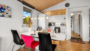 A modern kitchen with white cabinets, a dining area with a white table and black chairs, and a wooden ceiling. - "Sjarlotte" - 400m to the fjord by Interhome (Skjern)