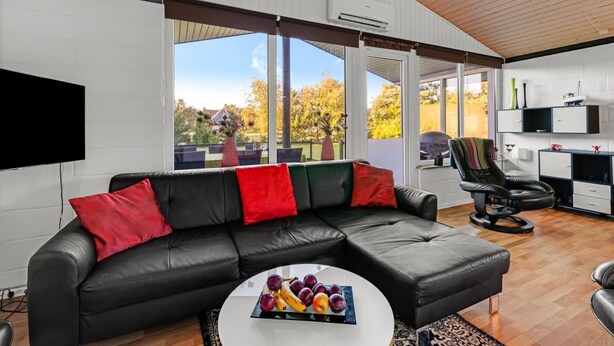 A modern living room with a black leather sofa, a round coffee table with fruit, and a view of the outdoors through large windows. - "Sjarlotte" - 400m to the fjord by Interhome (Skjern)
