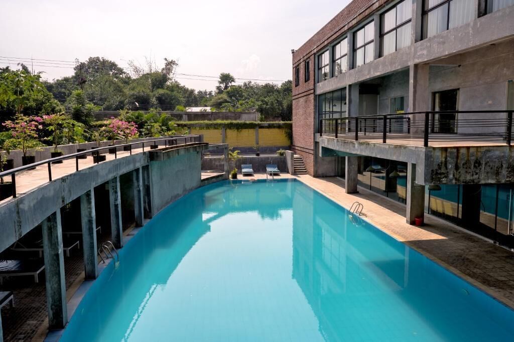 Una piscina con solárium de hormigón, rodeada por un edificio de grandes ventanales y fachada de ladrillo.