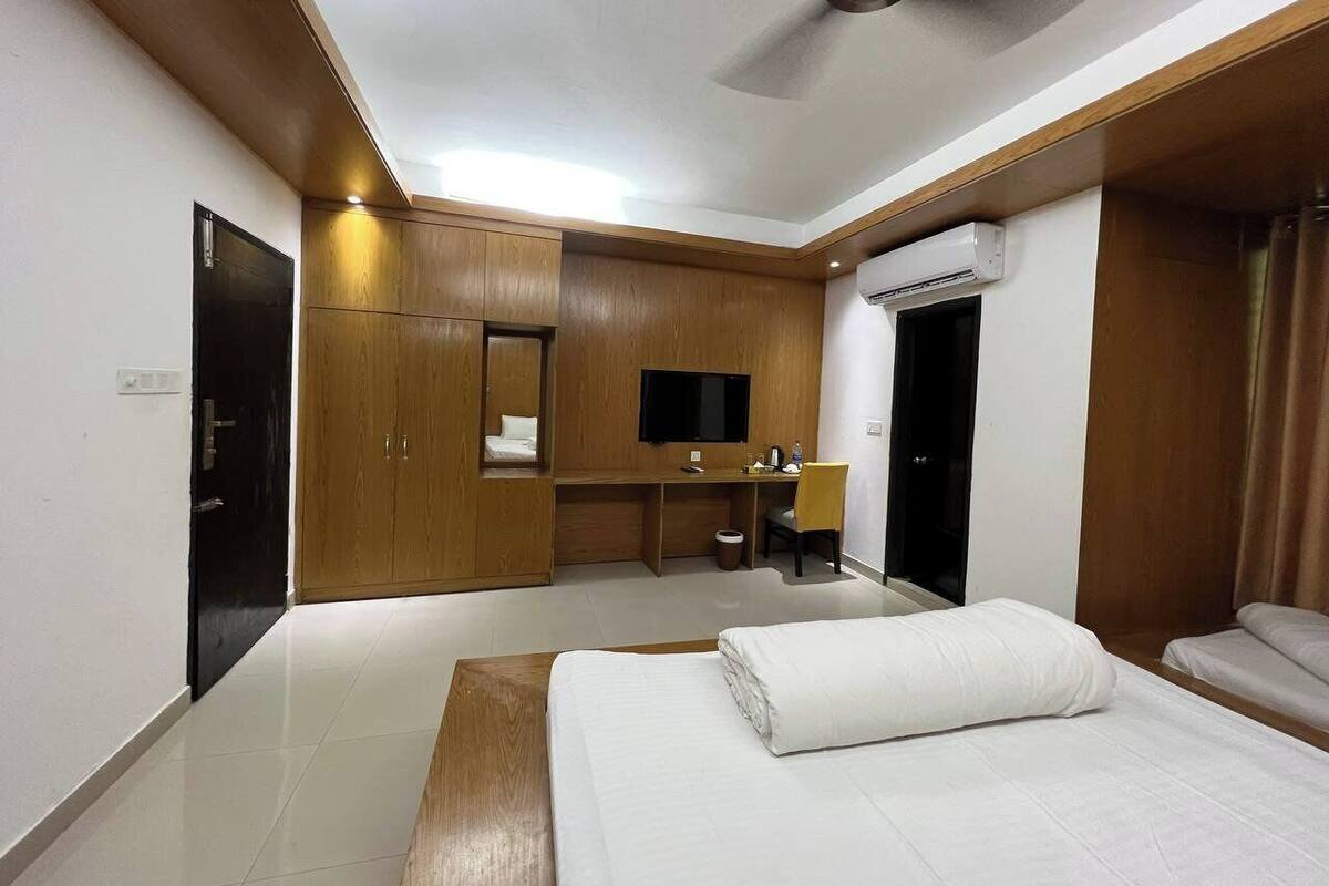 Habitación de hotel con cama, escritorio, silla, televisor y aire acondicionado.