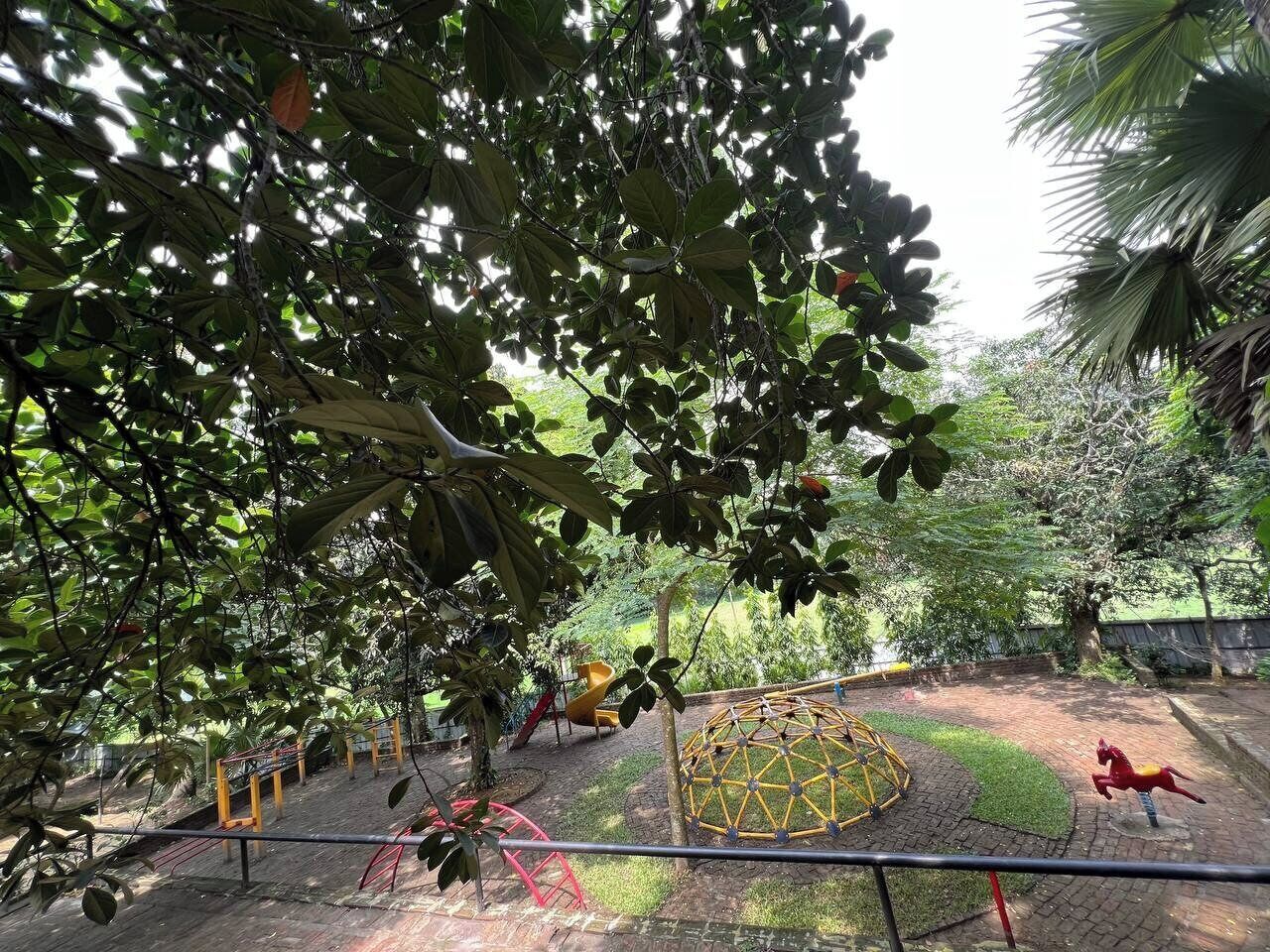 A playground with various play structures, including a slide and swings, surrounded by trees and greenery.