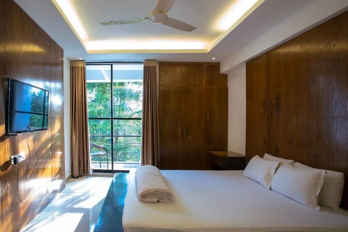 Una habitación de hotel moderna con una cama grande, un televisor de pantalla plana en la pared y un ventilador de techo.