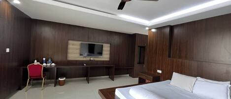 Una habitación de hotel moderna con una cama grande, un escritorio con una silla, un televisor montado en la pared y un ventilador de techo.