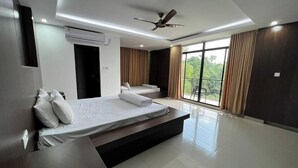 A modern hotel room with two beds, a ceiling fan, and large windows with curtains. - Chuti Resort Purbachal (Ulukhola)