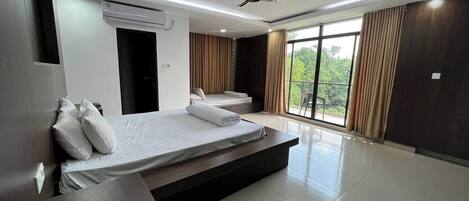 Quarto de hotel moderno com duas camas, ventoinha no teto e amplas janelas com cortinas.
