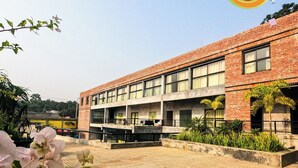 A two-story building with a brick facade, large windows, and a paved courtyard with plants. - Chuti Resort Purbachal (Ulukhola)
