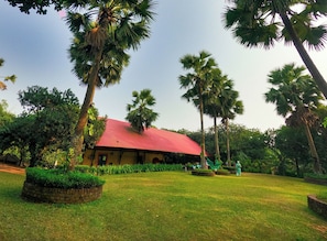 A resort with a red-roofed building surrounded by lush greenery and palm trees. - Chuti Resort Purbachal (Ulukhola)