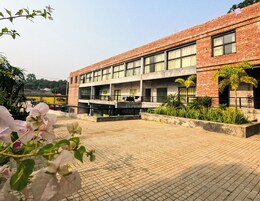 A two-story building with a brick facade, large windows, and a paved courtyard with plants.