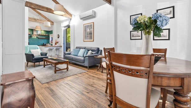 Una sala de estar con una mesa de comedor de madera, un sofá y una mesa de centro. Hay un jarrón con flores sobre la mesa.