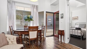 Un comedor con una mesa y sillas de madera, un florero con flores y vistas a través de una ventana con cortinas.