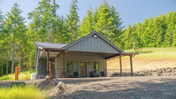 A cabin with a covered porch, a small outdoor seating area, and a gravel driveway.