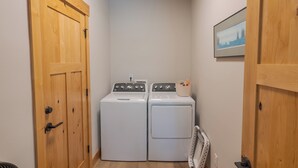 Une buanderie avec deux machines à laver blanches, des portes en bois et un tableau encadré au mur.