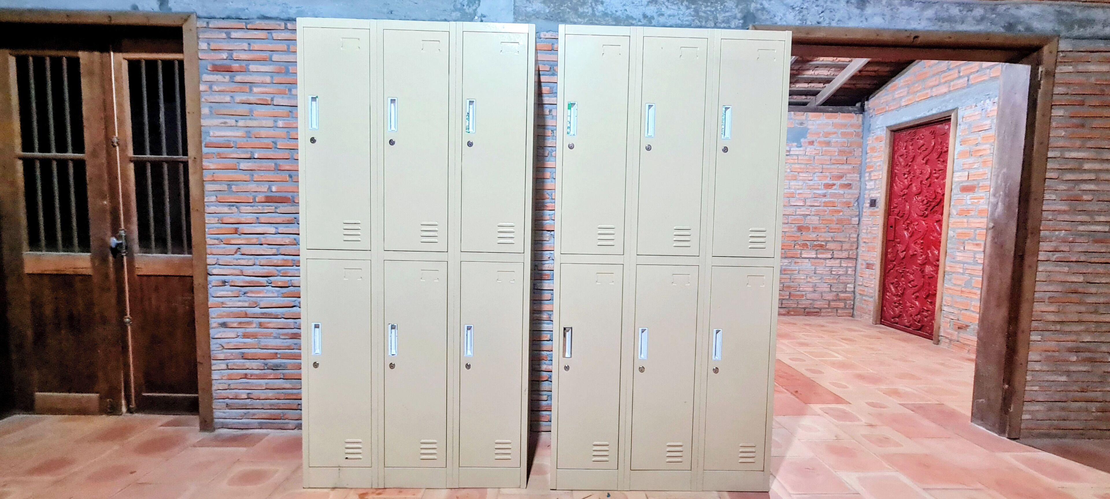 A set of beige metal lockers against a brick wall with a wooden door and a red decorative door.