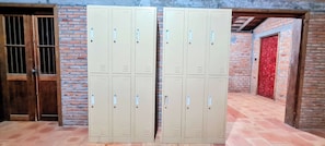 A set of beige metal lockers against a brick wall with a wooden door and a red decorative door. - Sun&Roots Lodge Restaurant and Bar (Kampot)
