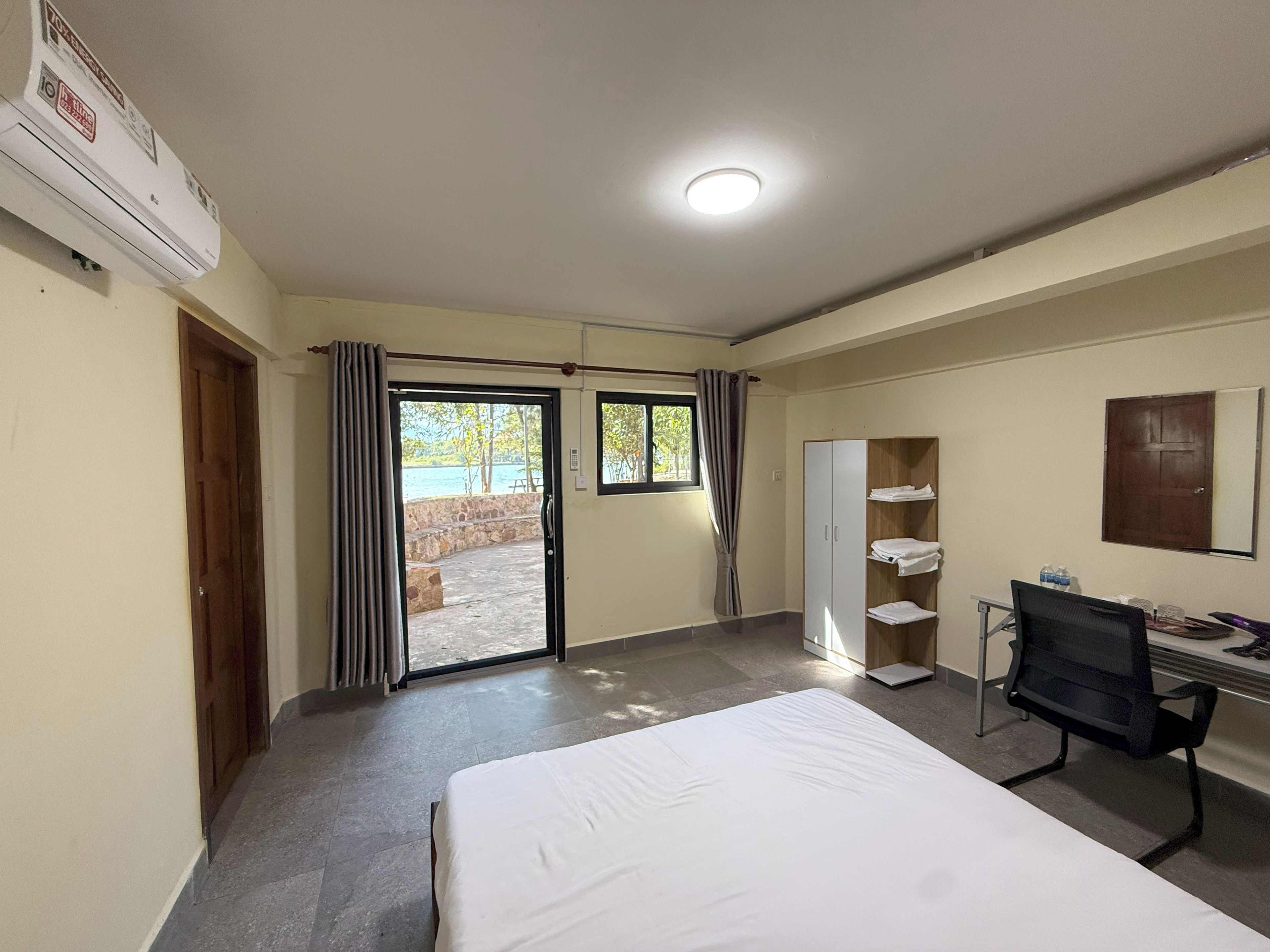 A hotel room with a bed, a desk, a chair, a wardrobe, and a view of the outdoors.