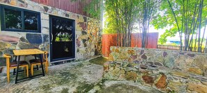 A stone wall with a wooden table and chairs, a black door, and a view of bamboo trees. - Sun&Roots Lodge Restaurant and Bar (Kampot)