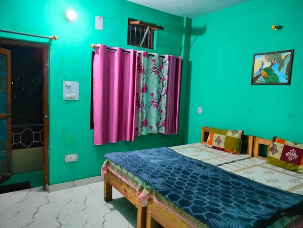 A room with a bed, a window with curtains, a wall-mounted electrical outlet, and a painting. - MangalMurti Himalyan Hotel (Almora)