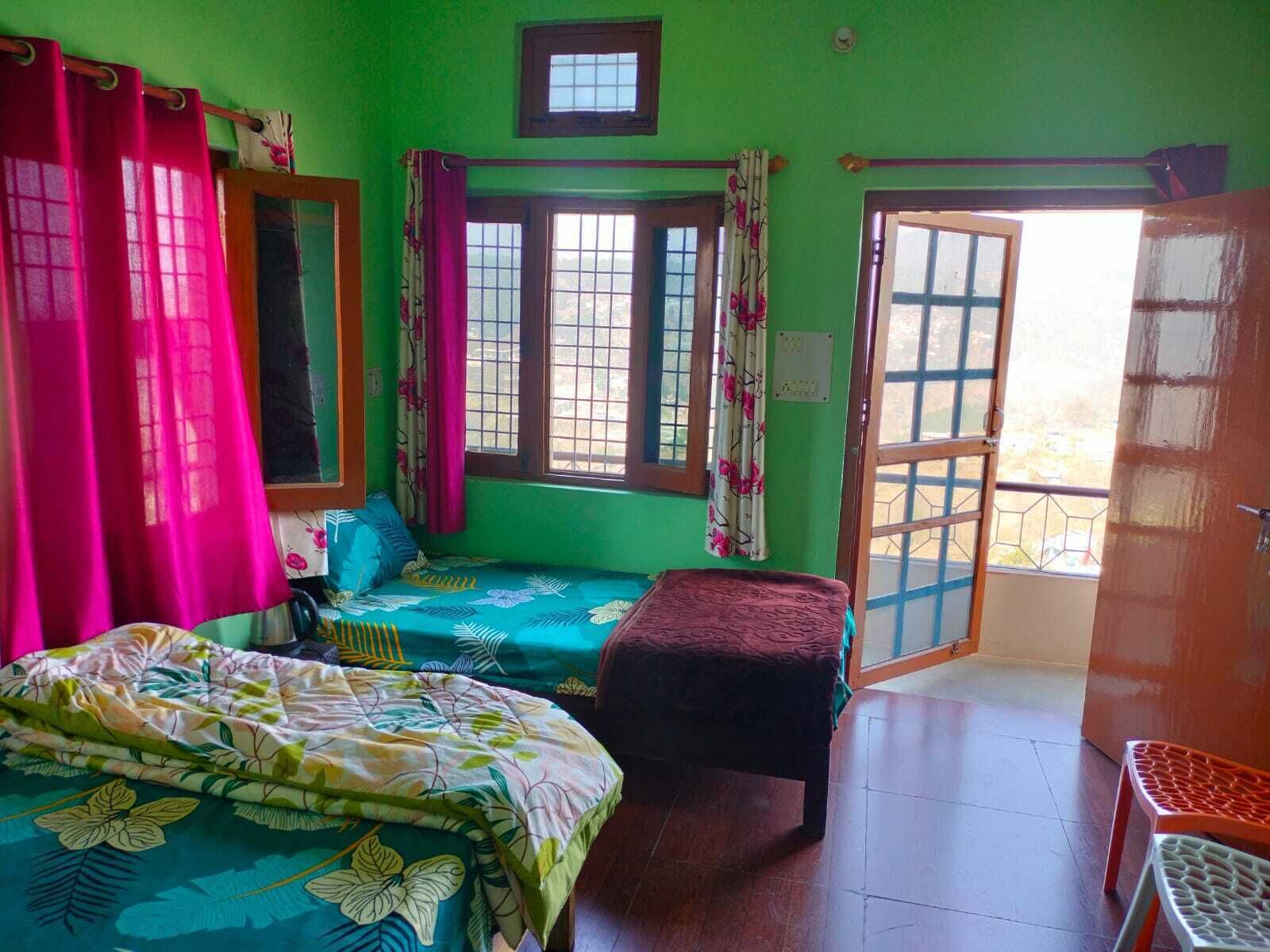 A room with two beds, a window with curtains, a small table, and a door leading outside.