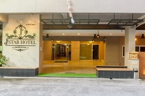 The entrance of a hotel with a marble facade, a sign with the hotel's name, and a foot wash station.