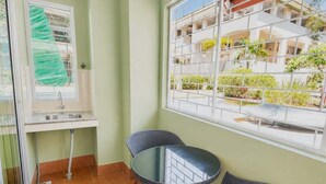 A room with a window, a sink, two chairs, and a view of a building with balconies.