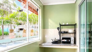 A small kitchen with a microwave, a shelf with dishes, and a window with a view of greenery.