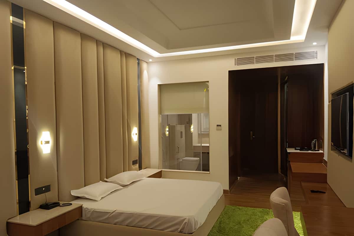 A modern hotel room with a large bed, bedside tables, a green rug, and a TV mounted on the wall.