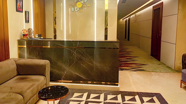 A modern hotel lobby with a reception desk, a sofa, a patterned rug, and a hallway with doors. - Hotel Maharaja Crest (Katra)