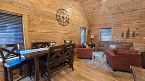 Un interior de cabaña acogedor con una mesa de comedor de madera, sillas, un sofá y un sillón.