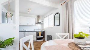 Una cocina moderna con armarios blancos, una campana extractora de acero inoxidable y una ventana con persianas.