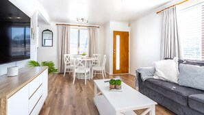 Una sala de estar moderna con televisor de pantalla plana, un comedor con mesa y sillas, un sofá gris y una mesa de centro de madera.
