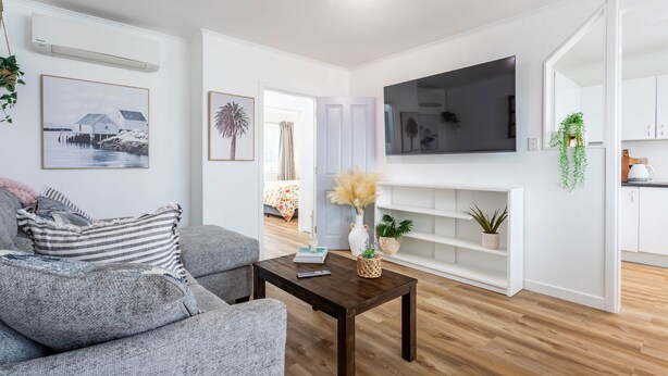 A modern living room with a grey sofa, a wooden coffee table, a TV mounted on the wall, and a white shelving unit. - Luxury Two-Bedroom Apartment (Upper Hutt)