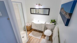 A bathroom with a white sink, toilet, and shower, a mirror above the sink, and a painting on the wall. - Luxury Two-Bedroom Apartment (Upper Hutt)