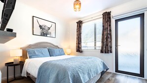 Een slaapkamer met een bed, nachtkastje, lamp, een lijst met foto en een schuifdeur van glas.