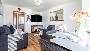 Een moderne woonkamer met een bank, fauteuils, een eettafel en een televisie.