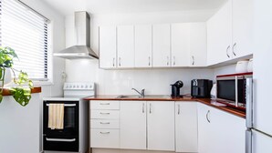 Een kleine keuken met witte kastjes, een inbouwoven, een magnetron en een koffiezetapparaat.
